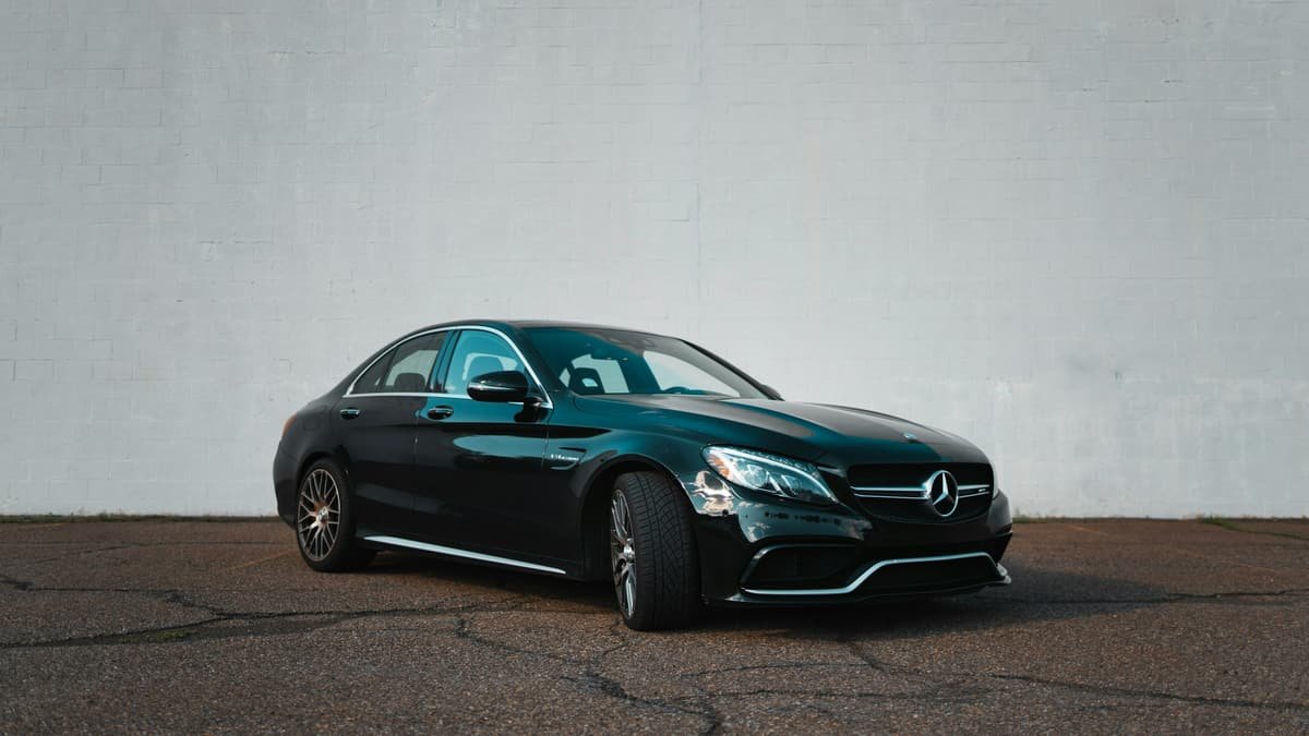 A black sedan parked against a white wall