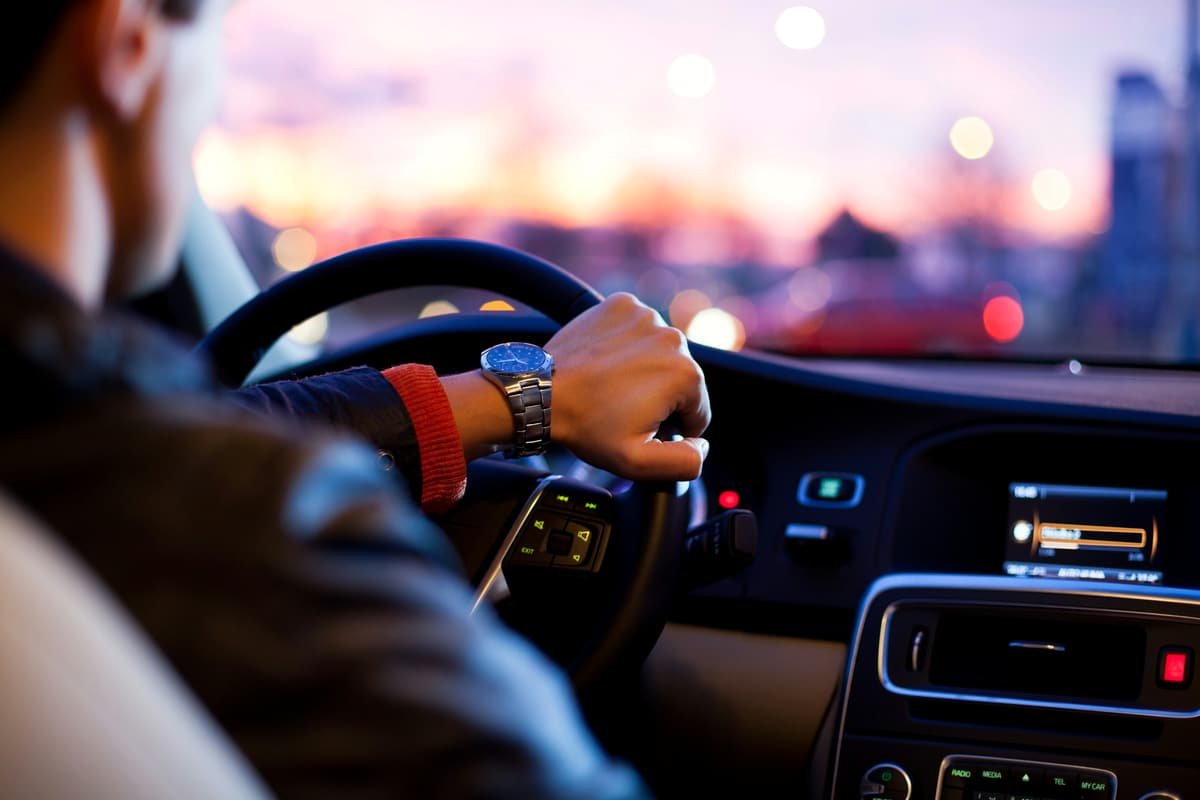 A chauffeur’s hands on the wheel at sunset